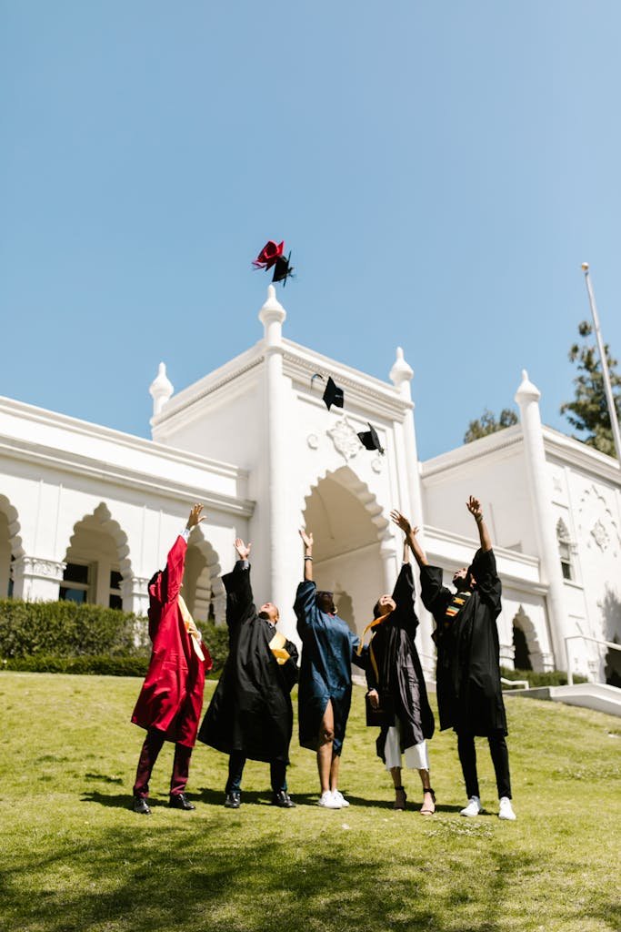 Group of graduates celebrating by tossing their caps outside a university building.
